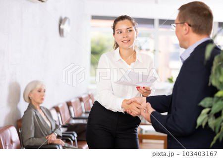 Young woman handshaking with other person in waiting room Young woman handshaking with other person in waiting room 103403167