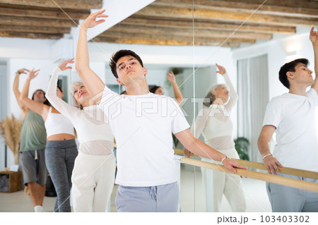 Young dancer man exercise near the ballet barre at a group training session in classical dance school. 103403302
