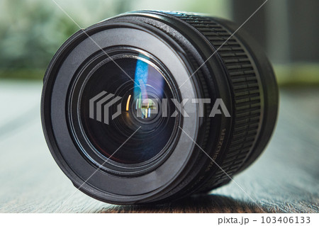 Front side view of a DSLR lens. Close-up. The 18-55mm zoom lens on a dark wooden background. Front side view of a DSLR lens. Close-up. The 18-55mm zoom lens on a dark wooden background. 103406133