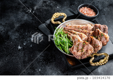Grilled Lamb mutton Chops steaks in a skillet with green salad. Black background. Top view. Copy space Grilled Lamb mutton Chops steaks in a skillet with green salad. Black background. Top view. Copy space 103414170