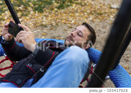 Man using smartphone while resting on swing outdoors 103417028