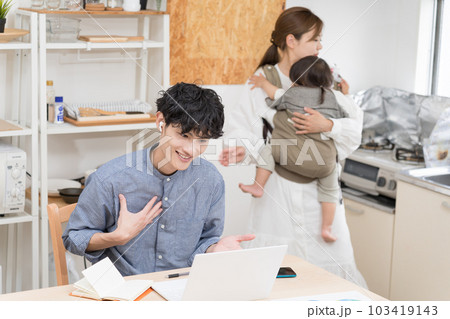 狭いダイニングキッチンで奥さんが家事と育児でバタバタする中、リモートワークする夫 103419143