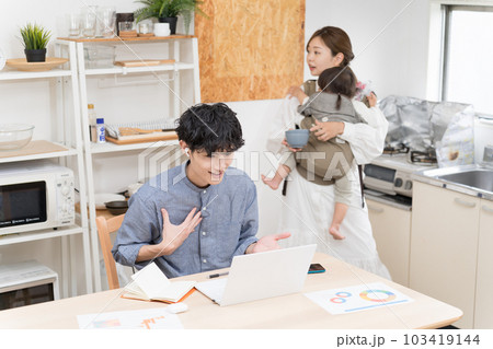 狭いダイニングキッチンで奥さんが家事と育児でバタバタする中、リモートワークする夫 103419144