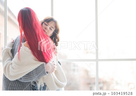 Two women dressed in sweaters sit by the window and gently hug. Lesbian intimacy. 103419528