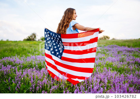 Young woman with american USA flag on blooming meadow. Independence Day, 4th July. Young woman with american USA flag on blooming meadow. Independence Day, 4th July. 103426782