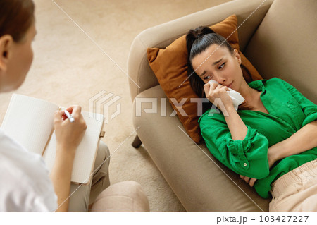 Top view of therapist making notes while female patient is lying on the couch and talking about her problems. 103427227