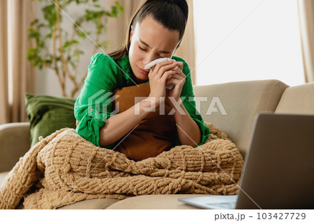 Young woman crying on couch in front of laptop. Young woman crying on couch in front of laptop. 103427729