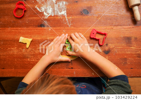 Hands of a toddler child cutting shaped biscuits out of dough on a brown wooden tabel. Christmas baking Hands of a toddler child cutting shaped biscuits out of dough on a brown wooden tabel. Christmas baking 103429224