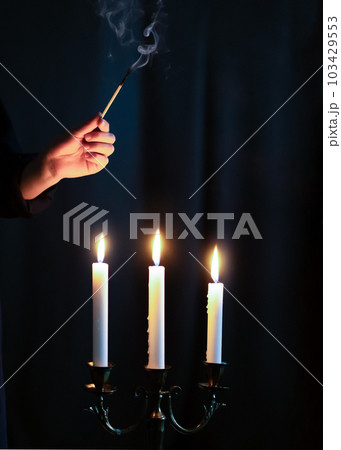 Hand igniting candles with match stick on the dark background. Condolence and mourning concept Hand igniting candles with match stick on the dark background. Condolence and mourning concept 103429553