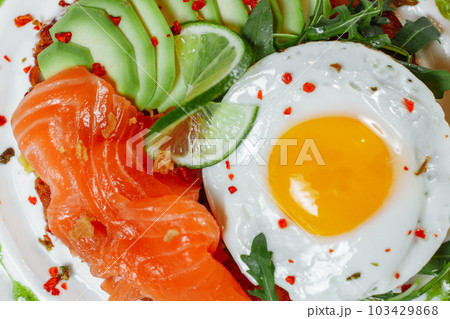 Poached eggs on top of smashed avocado on sourdough toast with smoked salmon. Healthy breakfast with plate on table. Top view. Copy space to right Poached eggs on top of smashed avocado on sourdough toast with smoked salmon. Healthy breakfast with plate on table. Top view. Copy space to right 103429868