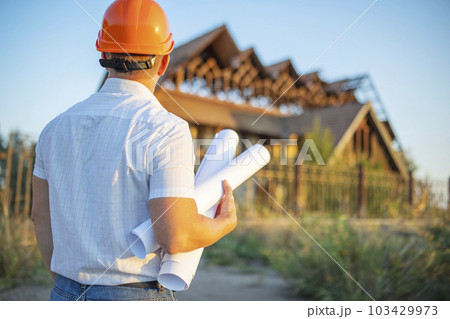 Young engineer in a yellow helmet with blueprints at a construction site Young engineer in a yellow helmet with blueprints at a construction site 103429973