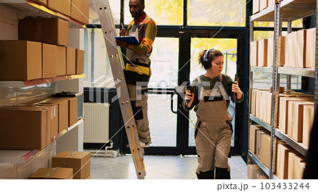 Young adult listening to music in depot, scanning barcodes of products and having fun in storage room. Woman dancing around warehouse and using scanner, quality control production. 103433244