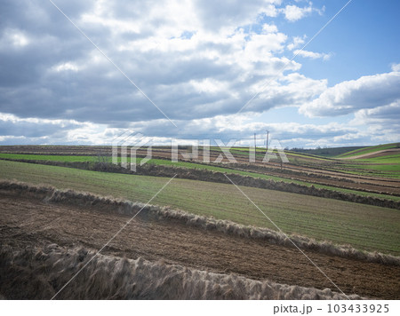 【ポーランド】郊外を走る鉄道の車窓から望む広大な田畑と雲が漂う空 103433925