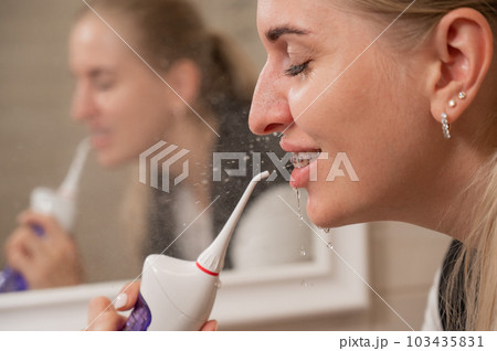 A woman with braces on her teeth uses an irrigator. Close-up portrait.  103435831