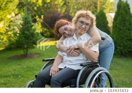 Caucasian woman hugging an elderly mother sitting in a wheelchair. Walk outdoors. Caucasian woman hugging an elderly mother sitting in a wheelchair. Walk outdoors. 103435832