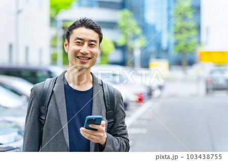 スマホを持って駐車場に立つ男性 103438755