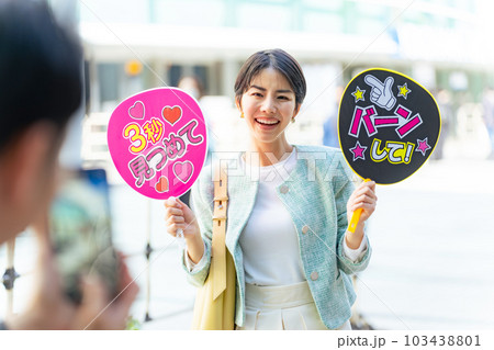 応援うちわを持ってコンサート会場の前に立つ女性　推し活 103438801