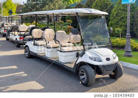 Golf cars parked at the edge of the lawn in the rays of the setting sun. 103439485