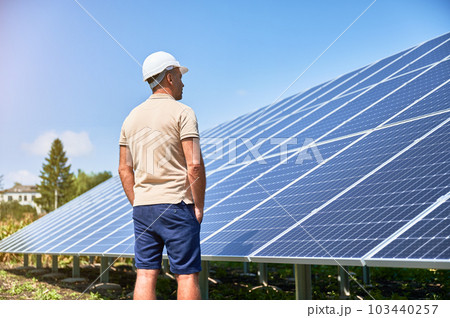 Back view of man in helmet next to solar system. Confident man looking at his investment. Male adult looking at photovoltaic batteries. 103440257