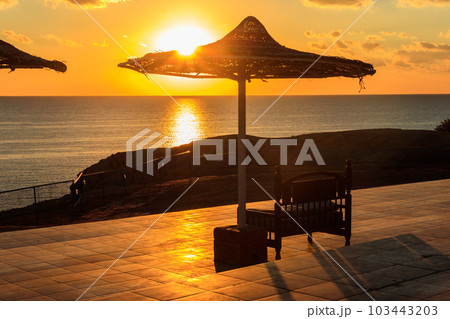 Cosy bench under beach sun umbrella with beautiful sea view at sunrise. Summer vacations concept 103443203