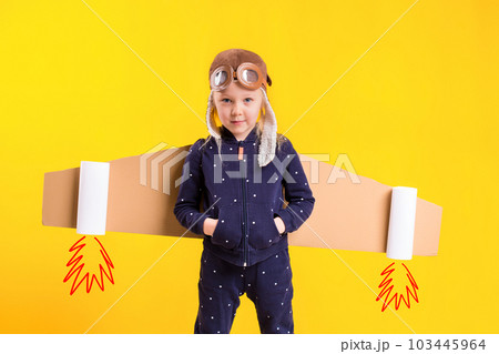 Freedom, girl playing to be airplane pilot, funny little girl with aviator cap and glasses, carries wings made of brown cardboard as an airplane Freedom, girl playing to be airplane pilot, funny little girl with aviator cap and glasses, carries wings made of brown cardboard as an airplane 103445964
