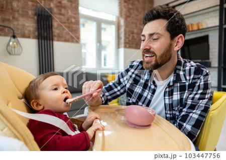 Father teaching his little baby to eat porridge from spoon infant daughter. Father teaching his little baby to eat porridge from spoon infant daughter. 103447756