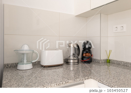 Close-up of a kitchen table with a juicer and kitchen appliances with white tiles and kitchen cabinets. The concept of household utensils and convenient gadgets for cooking 103450527