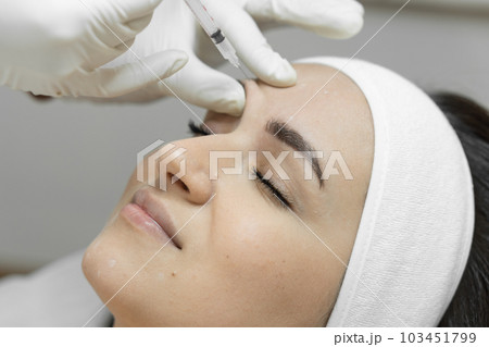 Injection with a syringe with butolin on a woman's face. Care with love: a woman visits a beautician for botulinum therapy, which makes her skin soft, smooth and youthful. Beauty clinic Injection with a syringe with butolin on a woman's face. Care with love: a woman visits a beautician for botulinum therapy, which makes her skin soft, smooth and youthful. Beauty clinic 103451799
