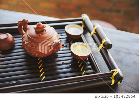 Brown ceramic pot and brown cup .Green tea on bamboo mat, aged wooden table Brown ceramic pot and brown cup .Green tea on bamboo mat, aged wooden table 103452954