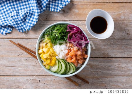Poke bowl with rice, salmon,cucumber,mango,onion,wakame salad, poppy seeds ands sunflowers seeds on wooden table Poke bowl with rice, salmon,cucumber,mango,onion,wakame salad, poppy seeds ands sunflowers seeds on wooden table 103453813