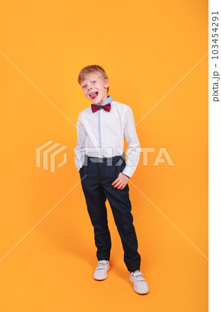 Full body portrait of smiling little boy in shirt with bowtie posing studio on yellow background 103454291