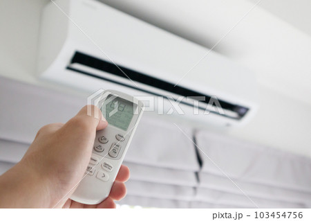 Hand with remote control directed on air conditioner 103454756