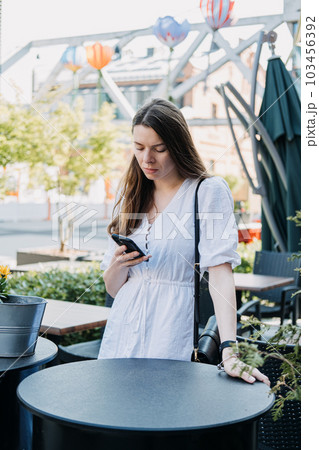 FOMO, Fear of missing out, social anxiety, stay continually connected, fear of regret, Social networking. Woman Checking her Smartphone and reading messengers and Social media outdoors 103456392