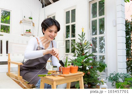 Smiling asian woman hold pot can watering green plant in office workplace. Happy female gardener or florist take care of domestic flowers. 103457701