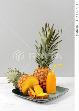 Slices of juicy pineapple and a fresh healthy smoothie in a glass bottle and a straw in a green plate on a wooden background. Healthy, detox and dietary nutrition concept. 103459683