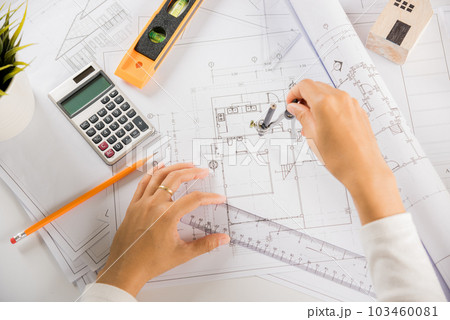 Architectural project workplace. Engineer sketching construction project, Architect drawing with divider compass on house plan blueprint paper for repair tools on table desk at architecture office Architectural project workplace. Engineer sketching construction project, Architect drawing with divider compass on house plan blueprint paper for repair tools on table desk at architecture office 103460081