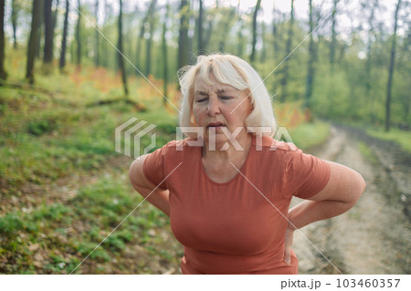 Back pain, an elderly woman has a muscle injury during exercise in nature. Caucasian fitness woman running s muscle back pain or cramps. High quality photo 103460357