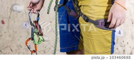 Young female climber holding carabiners for climbing, preparing for the climbing the wall in the climb center Young female climber holding carabiners for climbing, preparing for the climbing the wall in the climb center 103460698