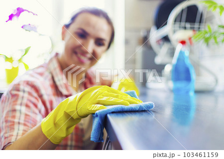 Housewife in yellow gloves wipes dust using spray detergent and rag 103461159