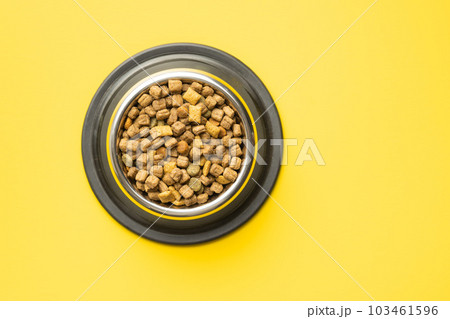 Dry kibble pet food. Dog or cat food in bowl on yellow background. Top view. Dry kibble pet food. Dog or cat food in bowl on yellow background. Top view. 103461596
