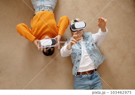 Attractive lesbian woman couple using vr goggles headset lying on floor 103462975