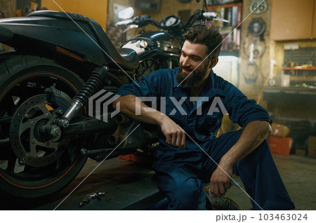 Satisfied smiling mechanic feeling glad looking at repaired motorcycle Satisfied smiling mechanic feeling glad looking at repaired motorcycle 103463024