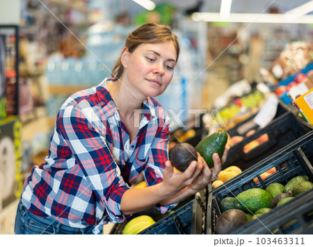 Young woman choosing ripe avocado on supermarket showcase 103463311