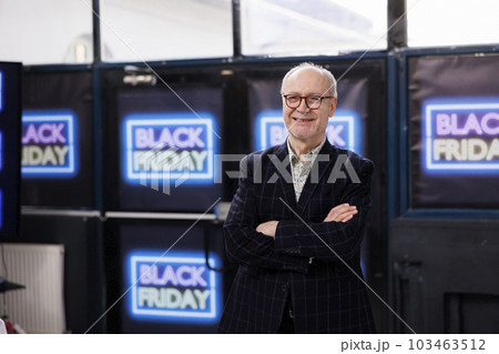 Happy senior man customer standing with crossed arms against neon Black Friday banners on wall in retail store, smiling at camera. People enjoying shopping during big sales Happy senior man customer standing with crossed arms against neon Black Friday banners on wall in retail store, smiling at camera. People enjoying shopping during big sales 103463512