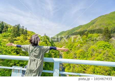 小安峡大噴湯　河原湯橋の上で春の風を感じる女性 103467435