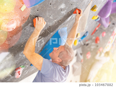 Alpinist practicing indoor rock climbing on artificial boulder without safety belts 103467882