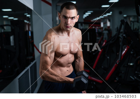 Shirtless man doing bicep exercises with dumbbells in the gym.  103468503