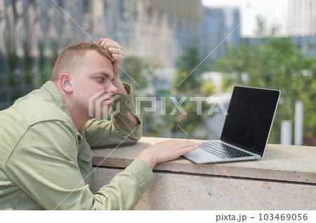 Sad guy with hearing aid using laptop outdoors.  103469056