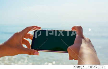 Close up photo of girls hands holding phone against the sea background Close up photo of girls hands holding phone against the sea background 103470872