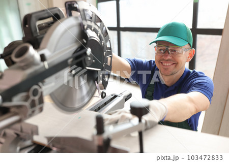 Carpenter with goggles cuts boards with sawing machine Carpenter with goggles cuts boards with sawing machine 103472833